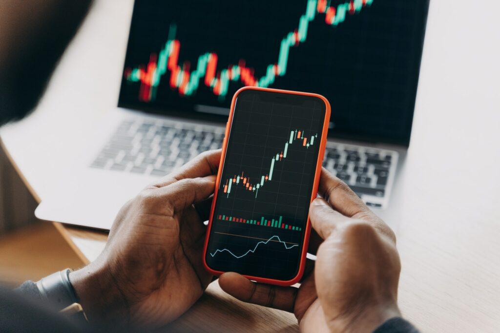 African man stock trader holding smartphone with financial charts and trading online investment data