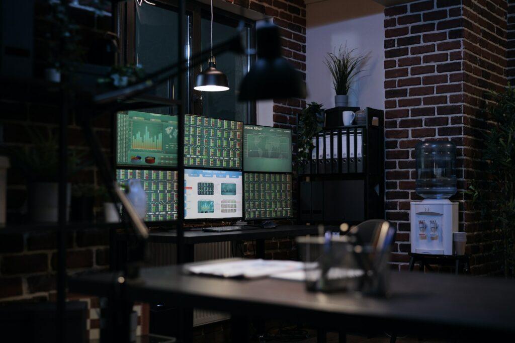 Interior of forex stock market workstation with multiple monitors and financial charts on displays.